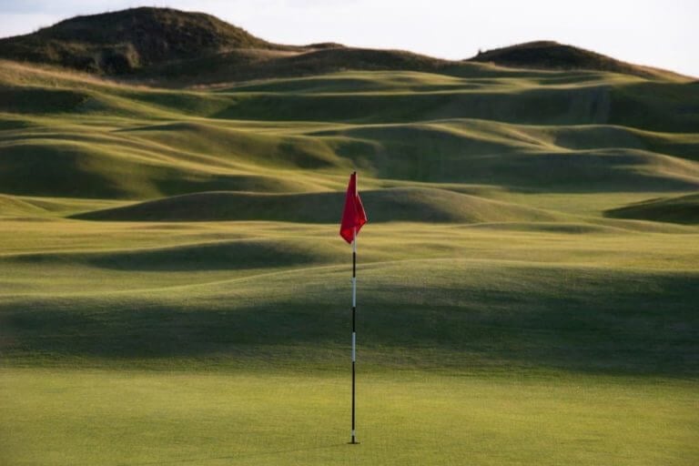 A flag stands on the fifth hole in front of rolling links terrain