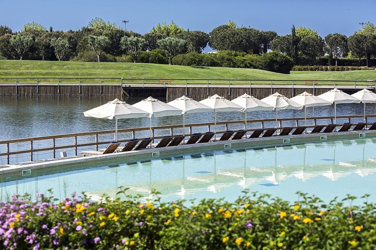 Sun recliners lined up in front of the naturally sand bottom pool