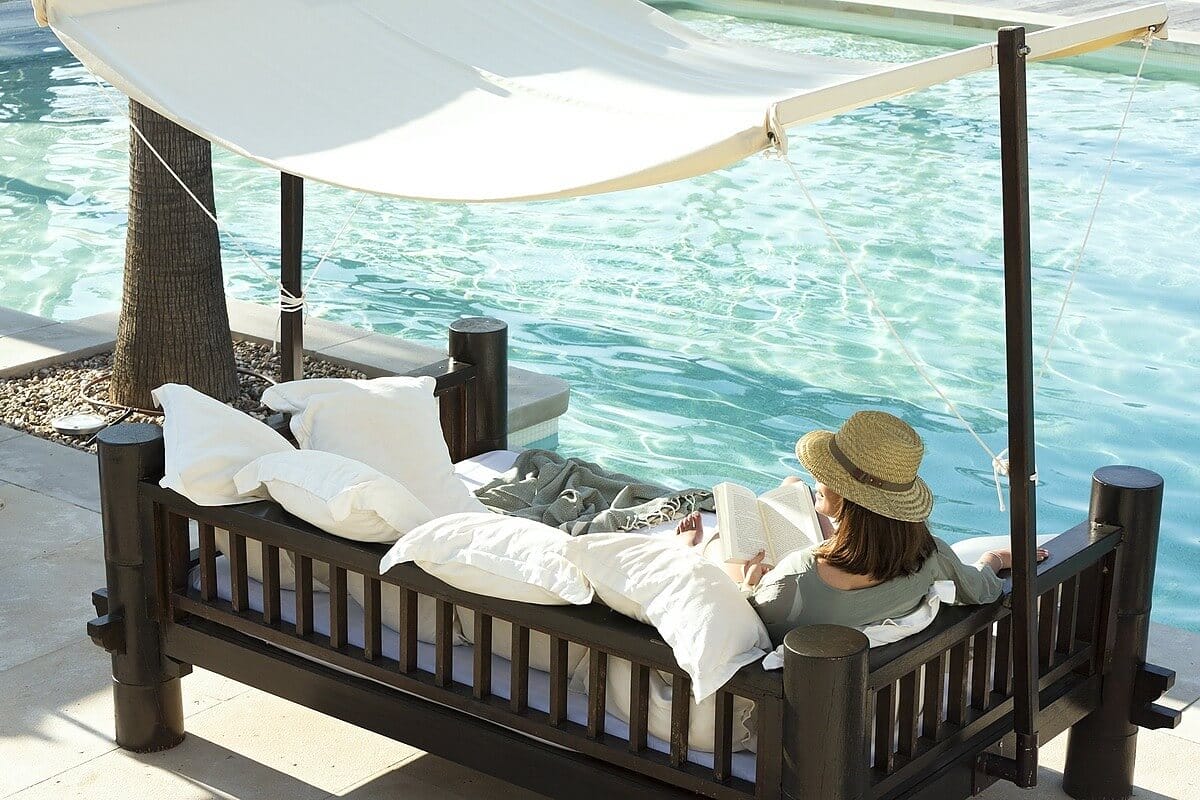 Woman reclines next to a pool reading a book