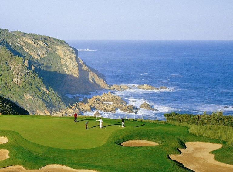 Golfers stand on the fourteenth green overlooking the Indian Ocean
